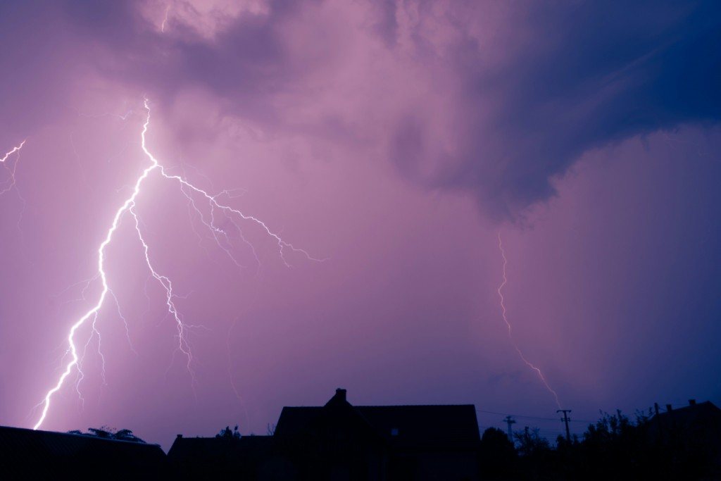 A stormy purple sky cut by a streak of lightning backlighting a residential home.