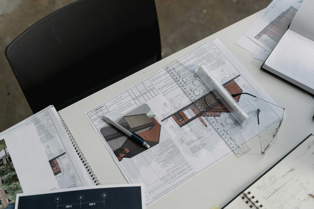 Overhead view of an architect’s desk with blueprints, a pen, a ruler, glasses, and notebooks.