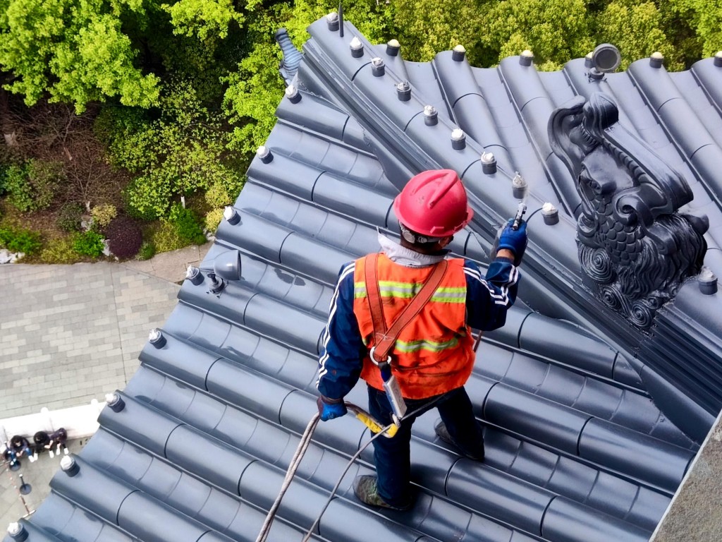 Worker wearing safety gear and helmet performing maintenance on a traditional tiled roof with decorative ridge details.