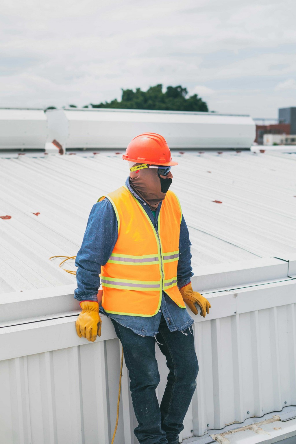 Construction worker in a safety vest and helmet standing on a metal roof during inspection or maintenance work.