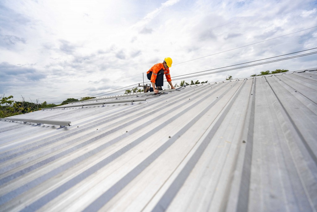 Roofing technician in safety gear installing a metal roof panel on a residential or commercial building
