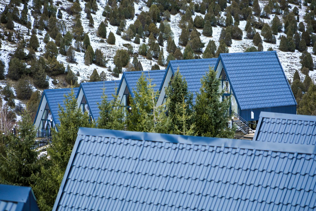 Row of A-frame cabins with blue roofs surrounded by pine trees and snowy hillside