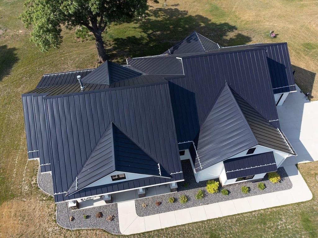 Aerial view of a residential home featuring a black standing seam metal roof with multiple roof sections and modern design.