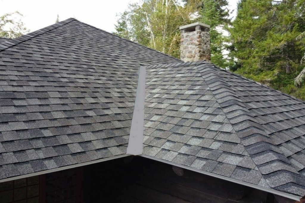 Residential home featuring a professionally installed architectural asphalt shingle roof with multiple roof slopes and a stone chimney.